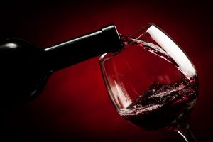 Pouring red wine in wine glass, red background