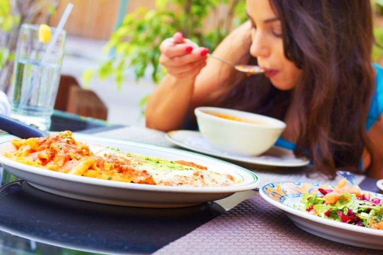 woman eating soup, pasta and salad in a restaurant