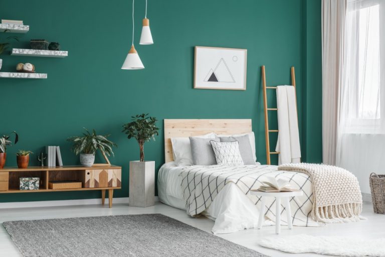 Bed between ladder and plant in green boho bedroom interior with grey carpet under lamps