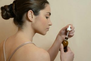 woman with her hair in a bun lifting a retinol serum dropper, examining it before application