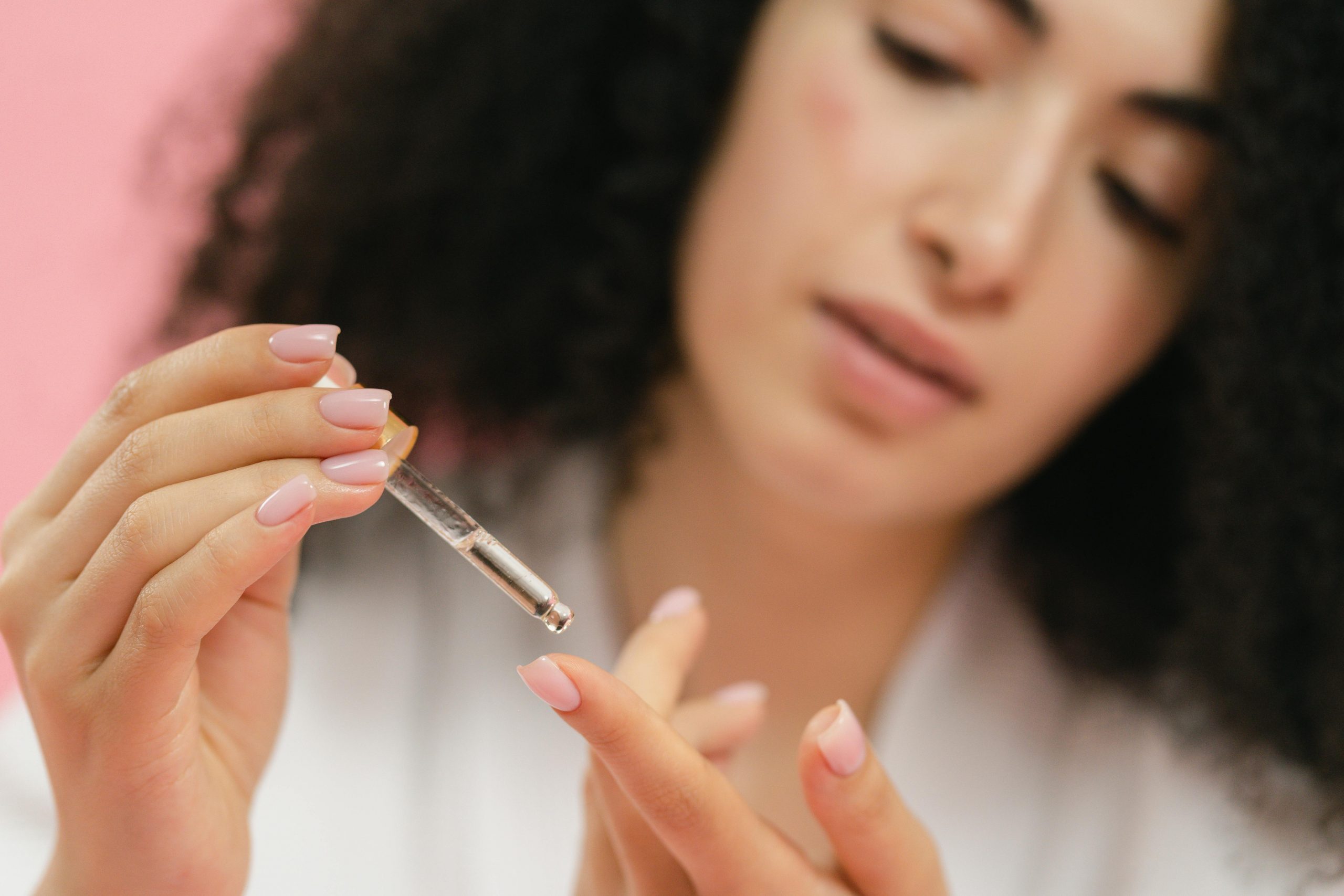 woman in a white bathrobe dispensing retinol serum onto her fingertip